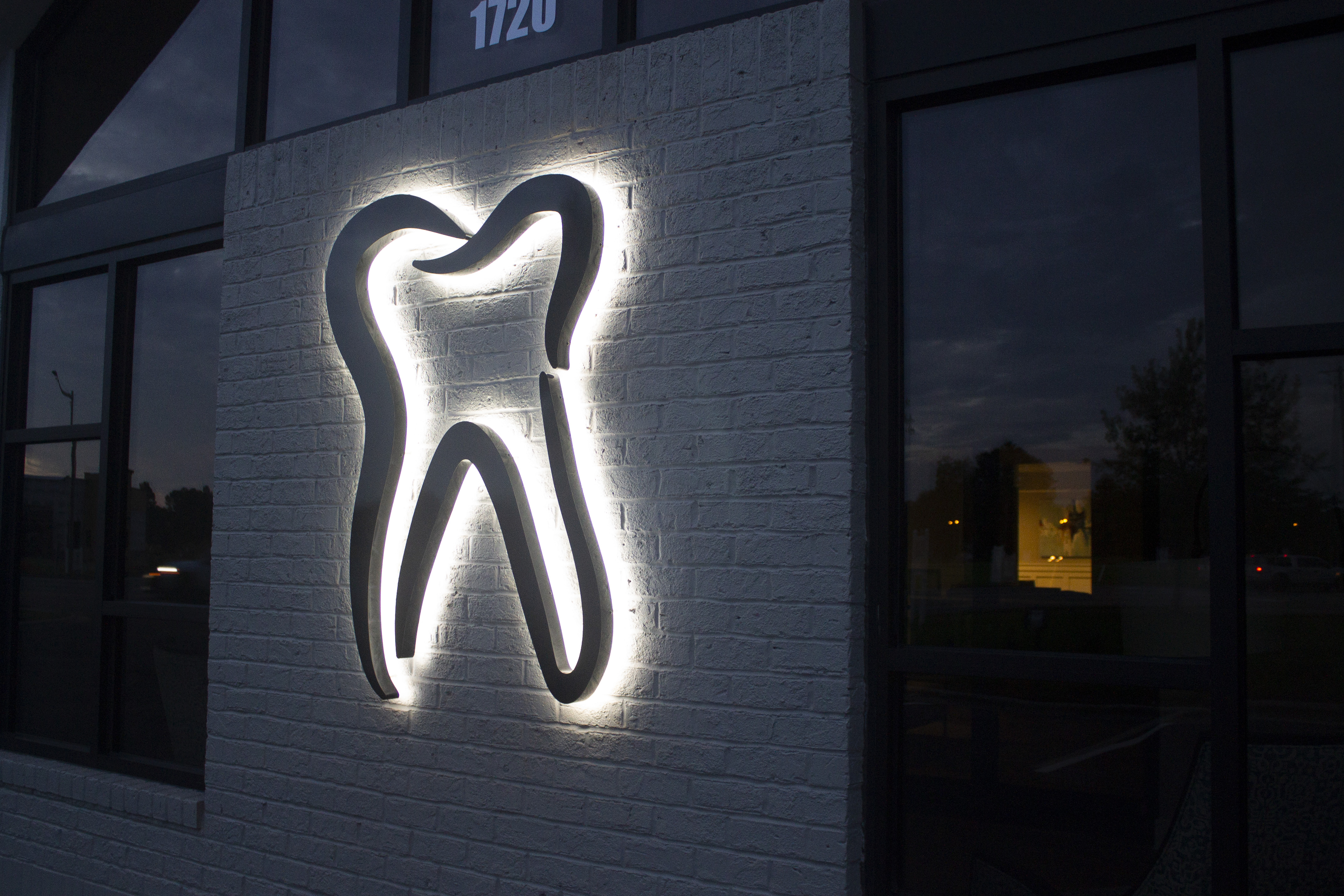 An custom lit-up sign of a tooth outside of a dental office, installed by FASTSIGNS